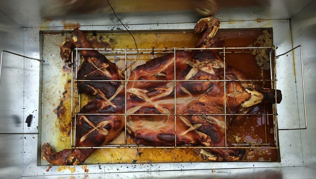 Chancho a la caja china dorándose lento sobre brasas, con la piel crocante