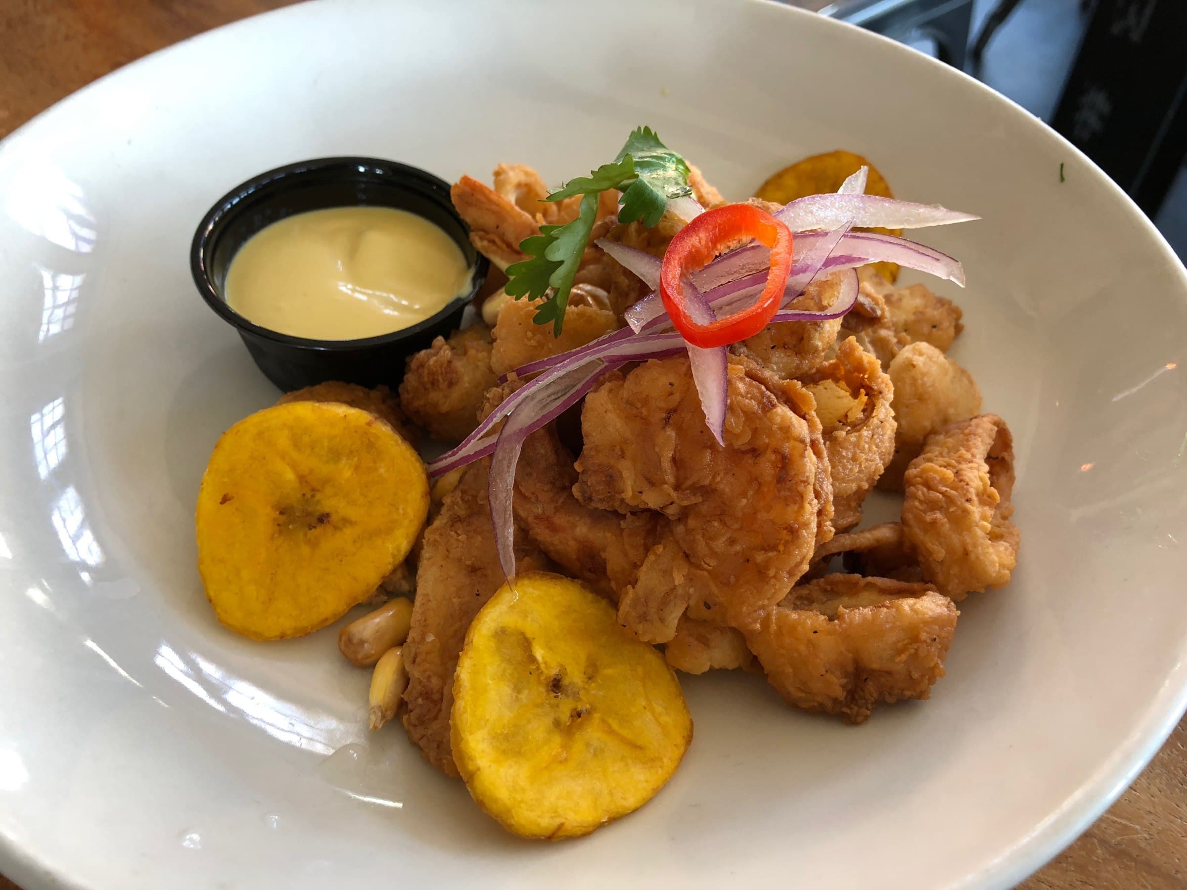 Chicharrón de trucha: trozos dorados y crocantes con yuca frita, sarsa criolla y salsa tártara en pote negro